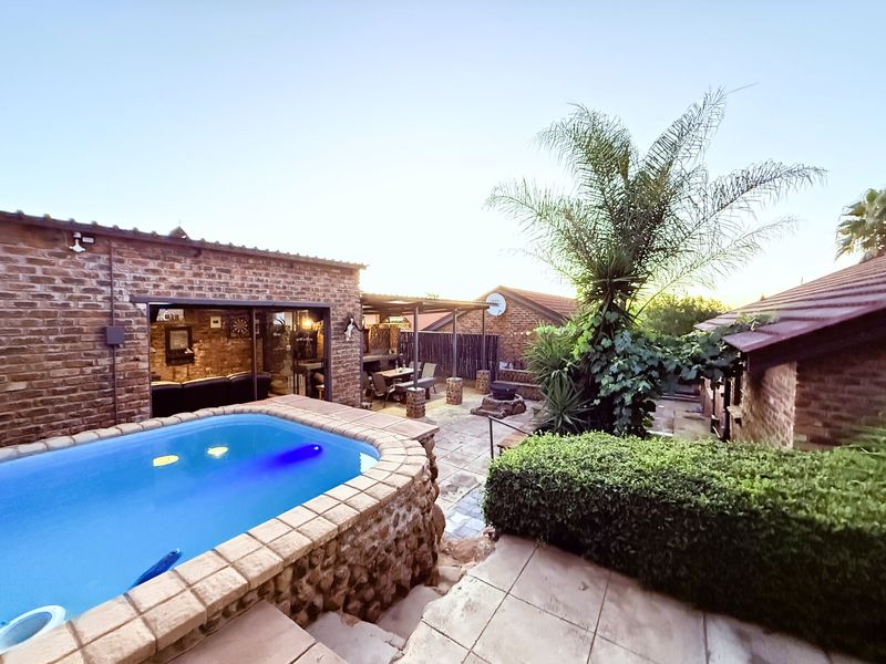 Outdoor entertainment area featuring a raised swimming pool with brick cladding, paved patio space, and a covered area adjacent to the main dwelling.