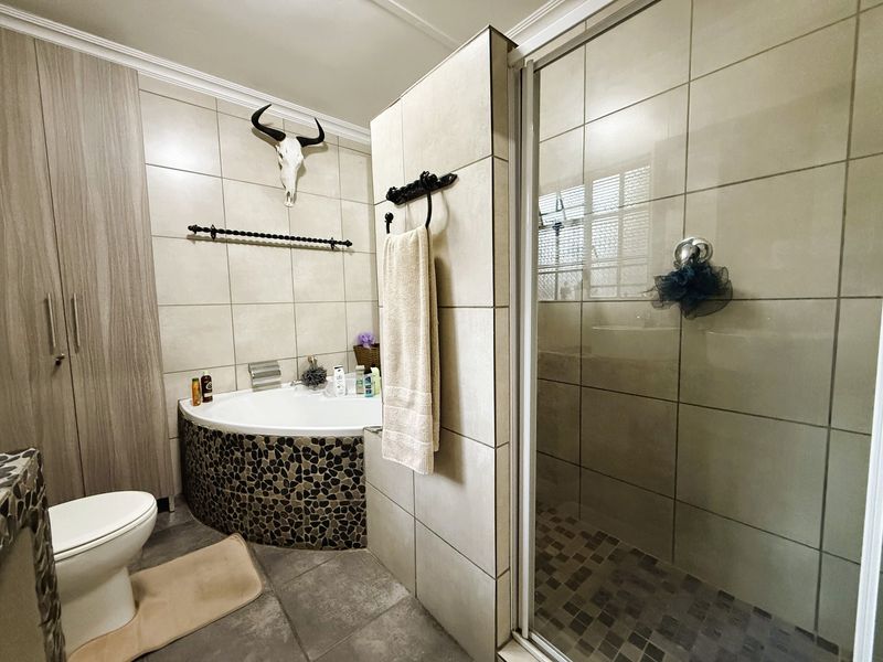A modern bathroom featuring a corner bathtub with stone-tiled surround, a separate glass-enclosed shower, and built-in storage cabinetry.