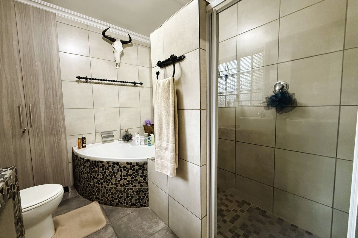A modern bathroom featuring a corner bathtub with stone-tiled surround, a separate glass-enclosed shower, and built-in storage cabinetry.