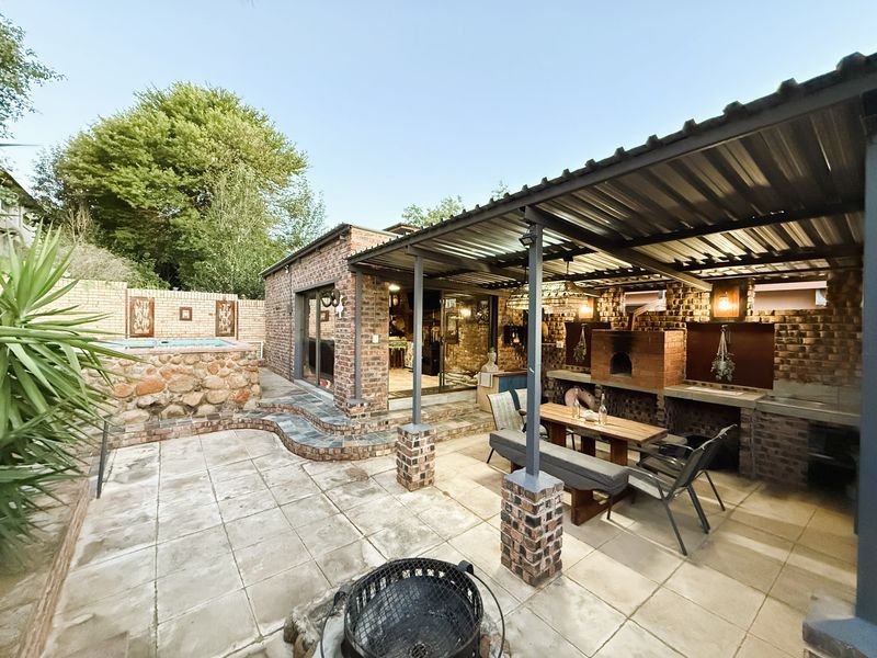 Covered outdoor patio featuring a built-in brick braai, paved flooring, and direct access to the home through sliding glass doors, adjacent to a stone-clad pool.