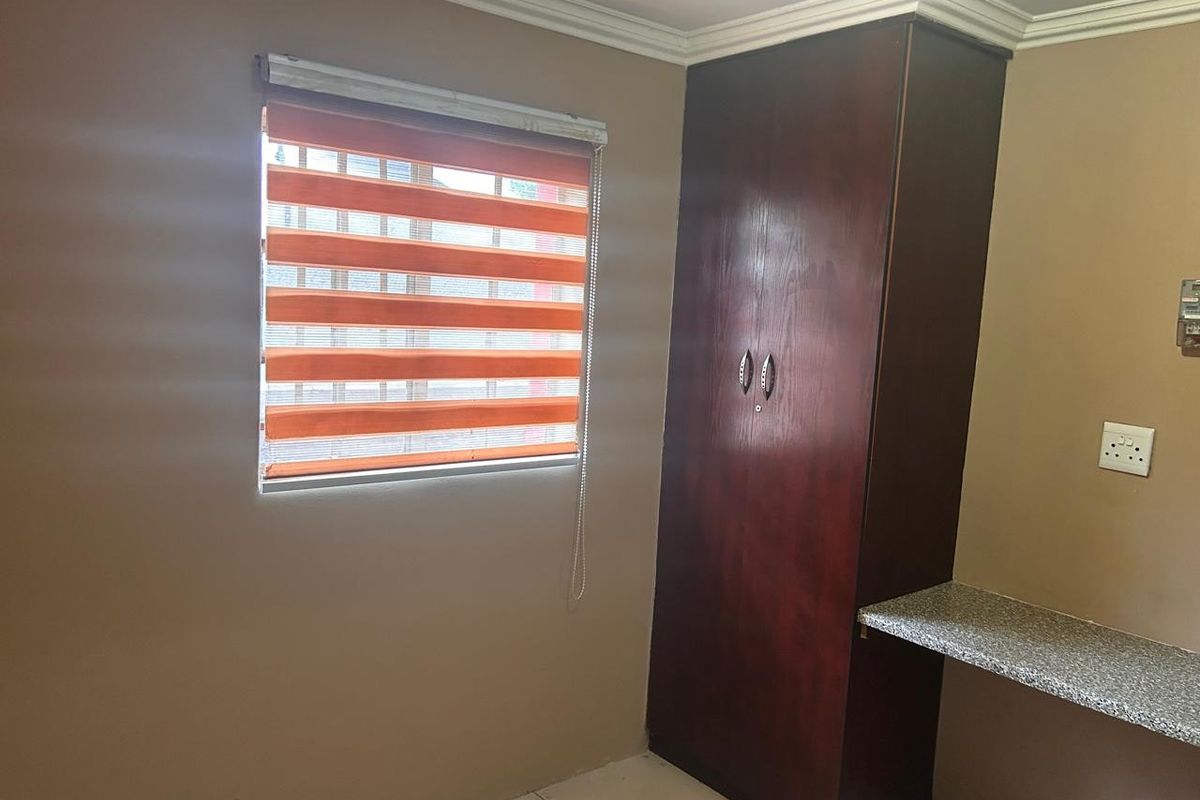 A bedroom featuring a built-in dark wood wardrobe, a stone-topped desk area, and a window fitted with modern striped roller blinds.