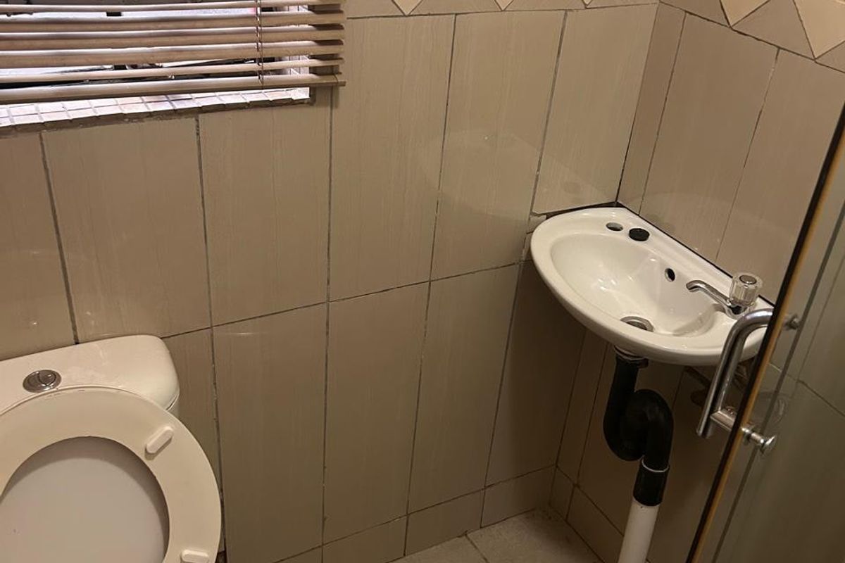 A compact bathroom featuring a wall-mounted corner basin, a standard toilet, and tiled wall finishes with a window blind.
