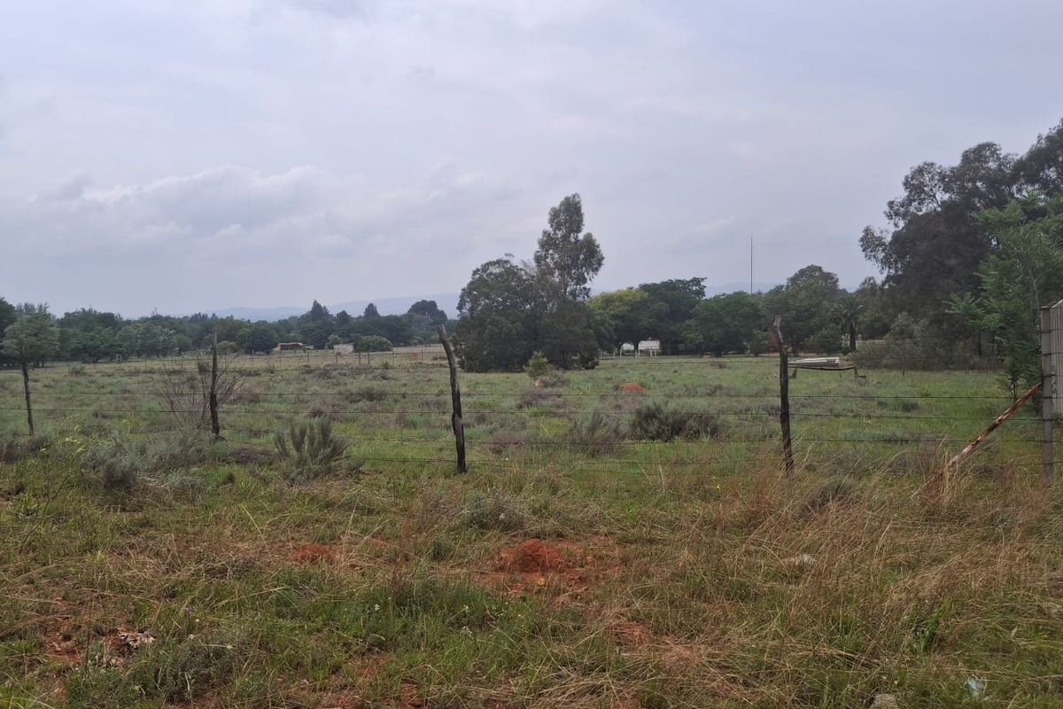A view of a vacant residential plot featuring natural grass, mature trees, and existing boundary fencing.