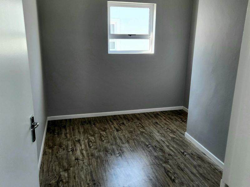 A clean, empty bedroom featuring modern grey walls and wood-look laminate flooring, providing a neutral canvas for personalization.