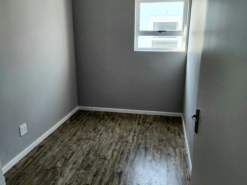 A clean, empty bedroom featuring modern grey walls and wood-look laminate flooring, providing a neutral canvas for personalization.