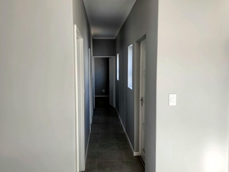 A clean, neutral-toned hallway featuring tiled flooring and coved cornicing, providing access to multiple rooms within the home.