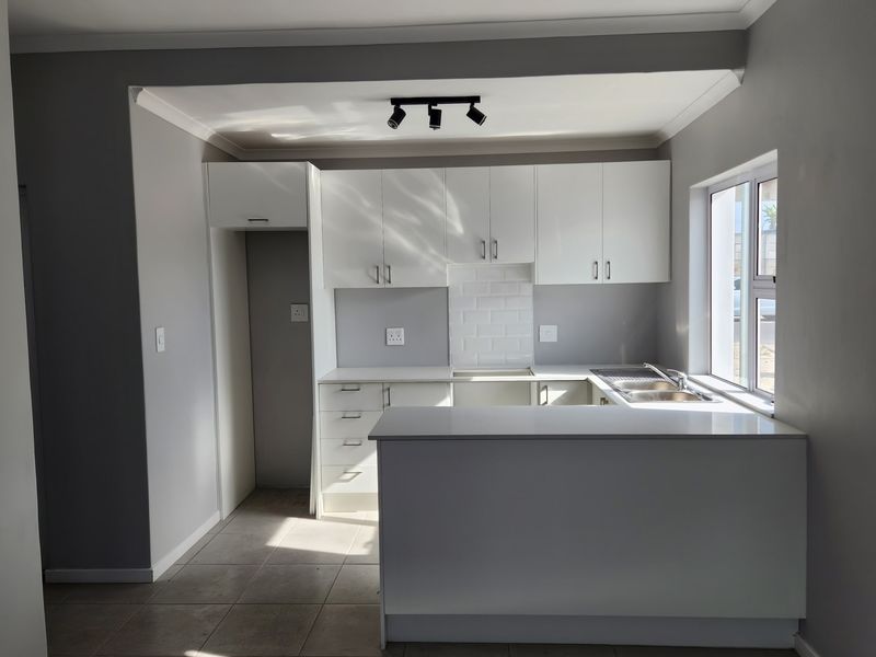 Modern kitchen featuring white cabinetry, subway tile backsplash, double bowl sink, and a breakfast bar, finished with neutral tiled flooring.
