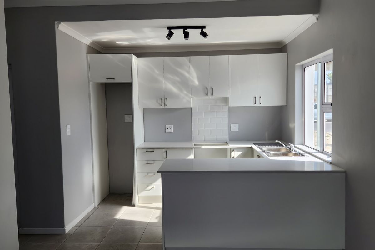 Modern kitchen featuring white cabinetry, subway tile backsplash, double bowl sink, and a breakfast bar, finished with neutral tiled flooring.