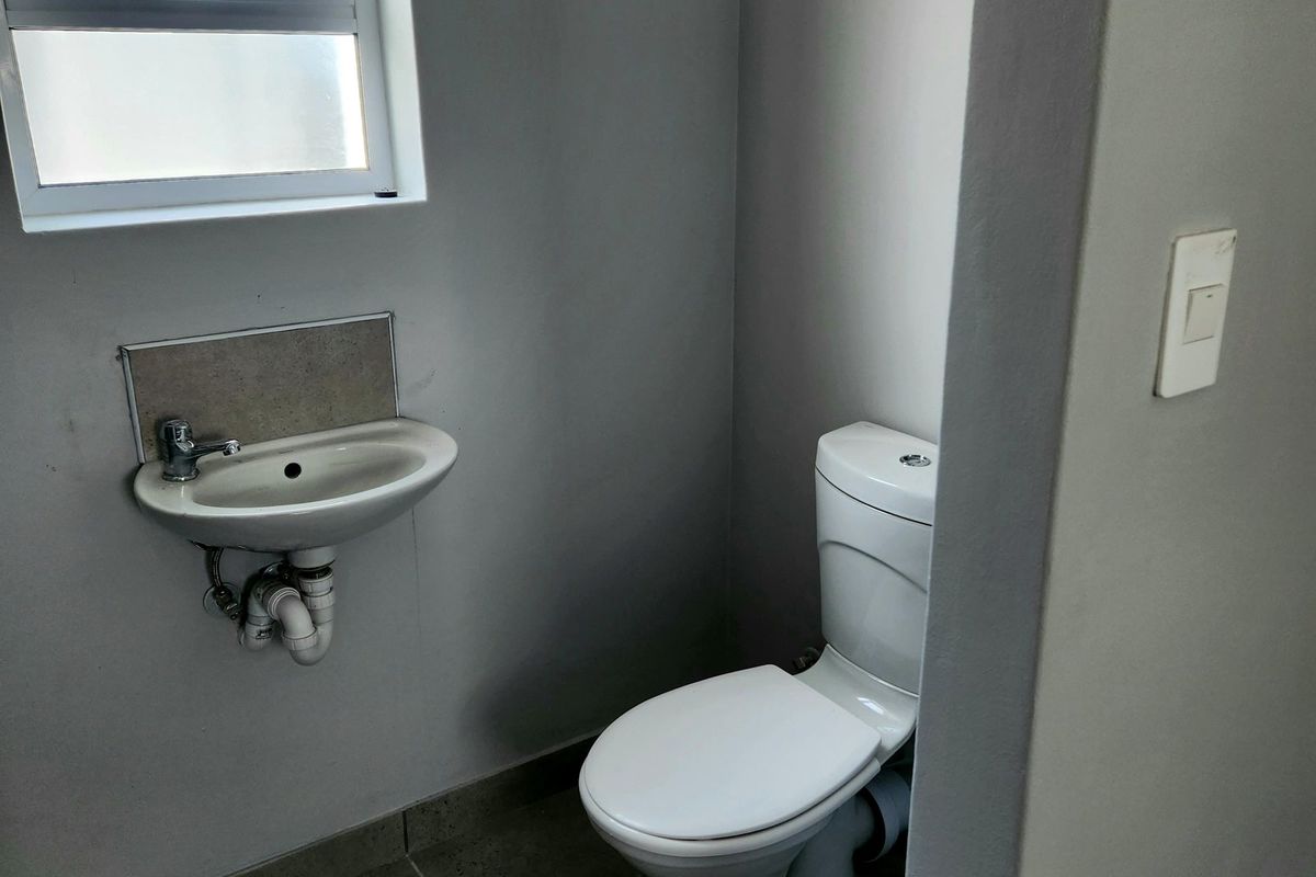 A compact guest bathroom featuring a wall-mounted basin, toilet, and tiled flooring with a frosted window for natural light.
