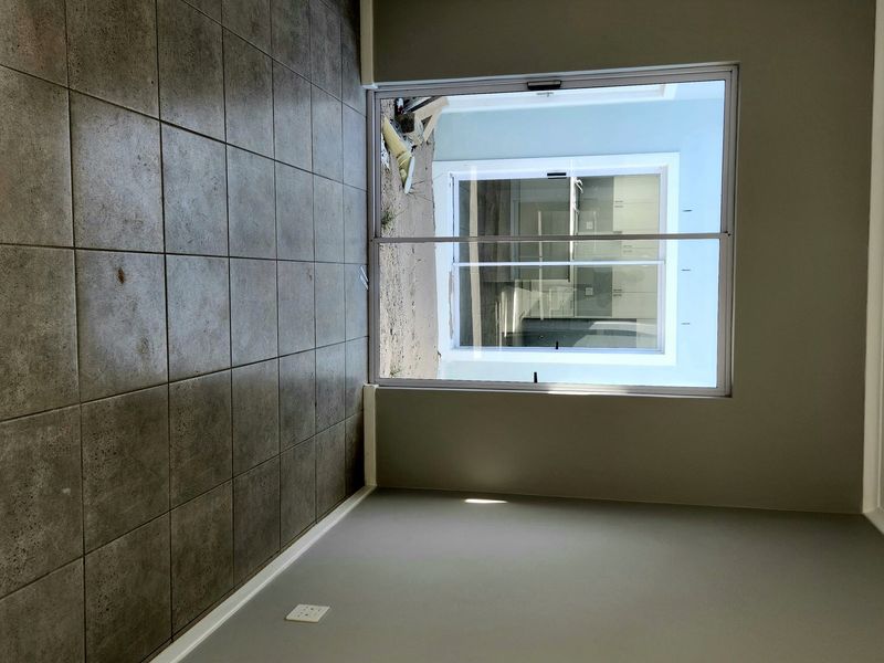 An empty living room featuring neutral grey walls, ceramic tiled flooring, and a large sliding glass door providing access to the exterior.