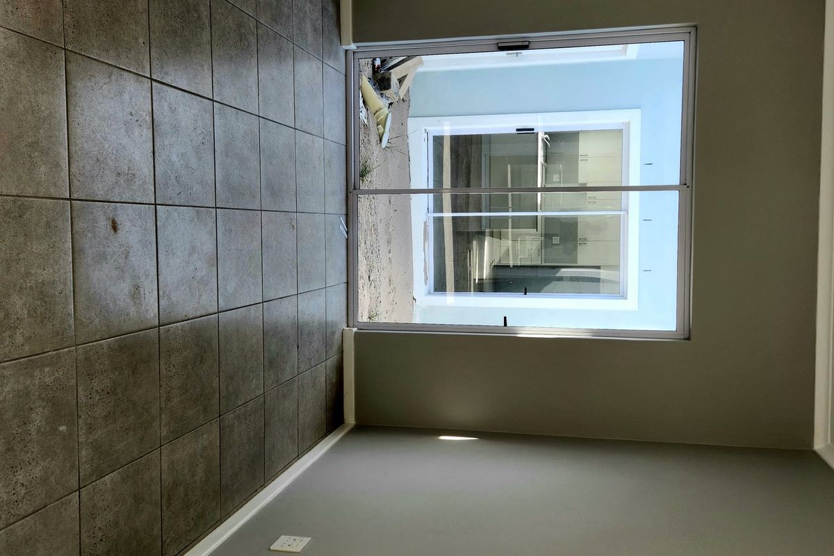 An empty living room featuring neutral grey walls, ceramic tiled flooring, and a large sliding glass door providing access to the exterior.