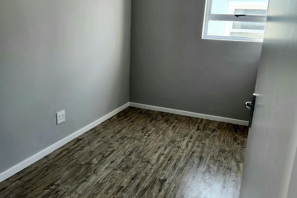 A clean, empty bedroom featuring modern grey walls, wood-look laminate flooring, and a single casement window providing natural light.