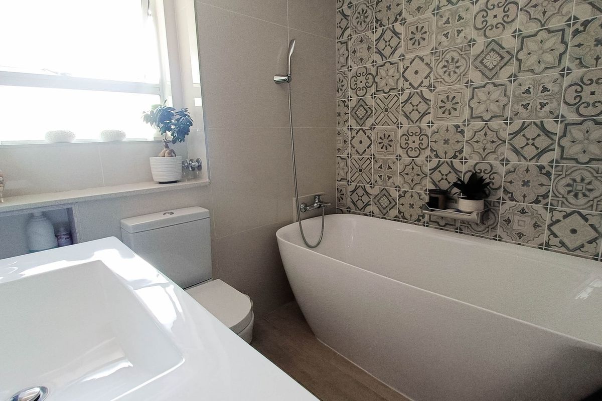 Modern bathroom featuring a sleek freestanding bathtub, patterned feature wall tiles, a vanity basin, and a toilet with natural light from the window.