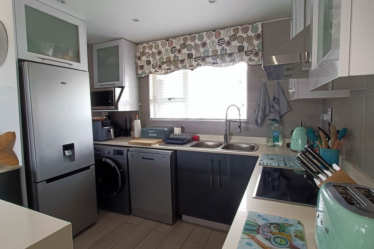 A functional kitchen featuring modern dark cabinetry, light countertops, tiled backsplash, and integrated appliances including a hob and extractor fan.