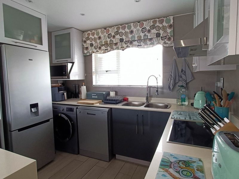 A functional kitchen featuring modern dark cabinetry, light countertops, tiled backsplash, and integrated appliances including a hob and extractor fan.