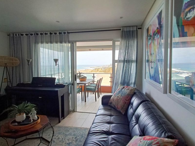 Bright living room featuring tiled flooring and large sliding glass doors that open onto a balcony with scenic ocean views.