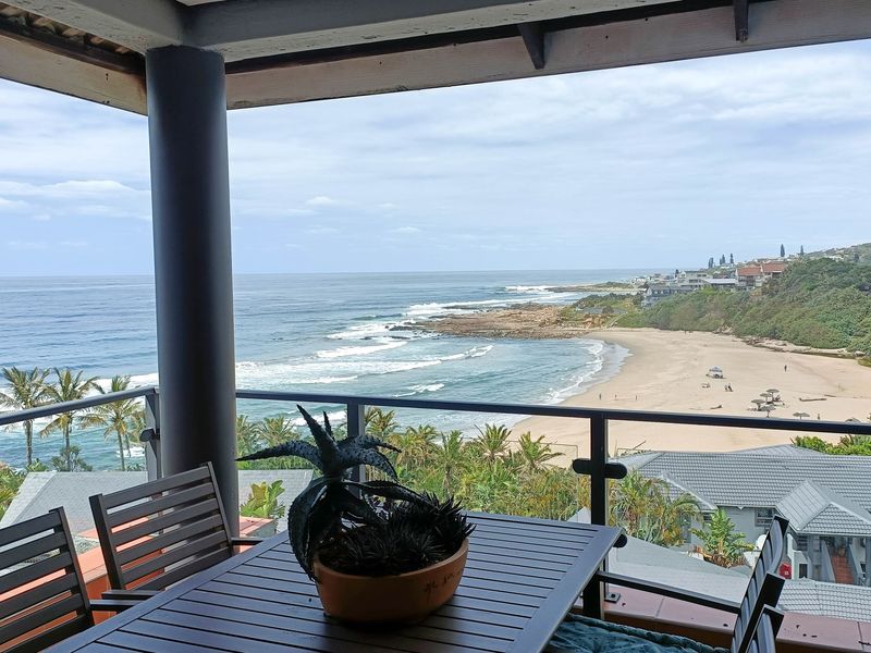 A spacious covered balcony featuring a metal railing and offering expansive, unobstructed views of the coastline and beach.