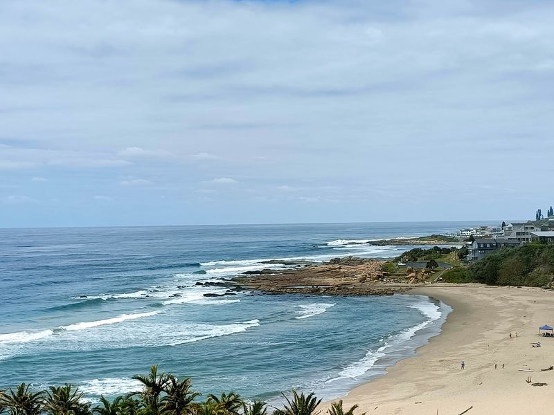 A scenic coastal view overlooking the sandy beach, rocky shoreline, and ocean waves.