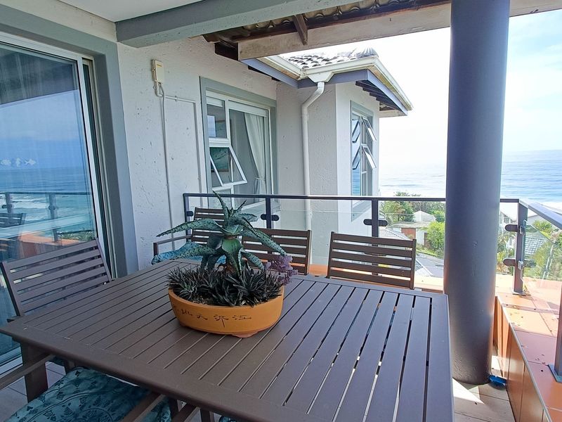 A spacious covered balcony featuring a glass balustrade and direct ocean views, providing a seamless transition between indoor and outdoor living spaces.