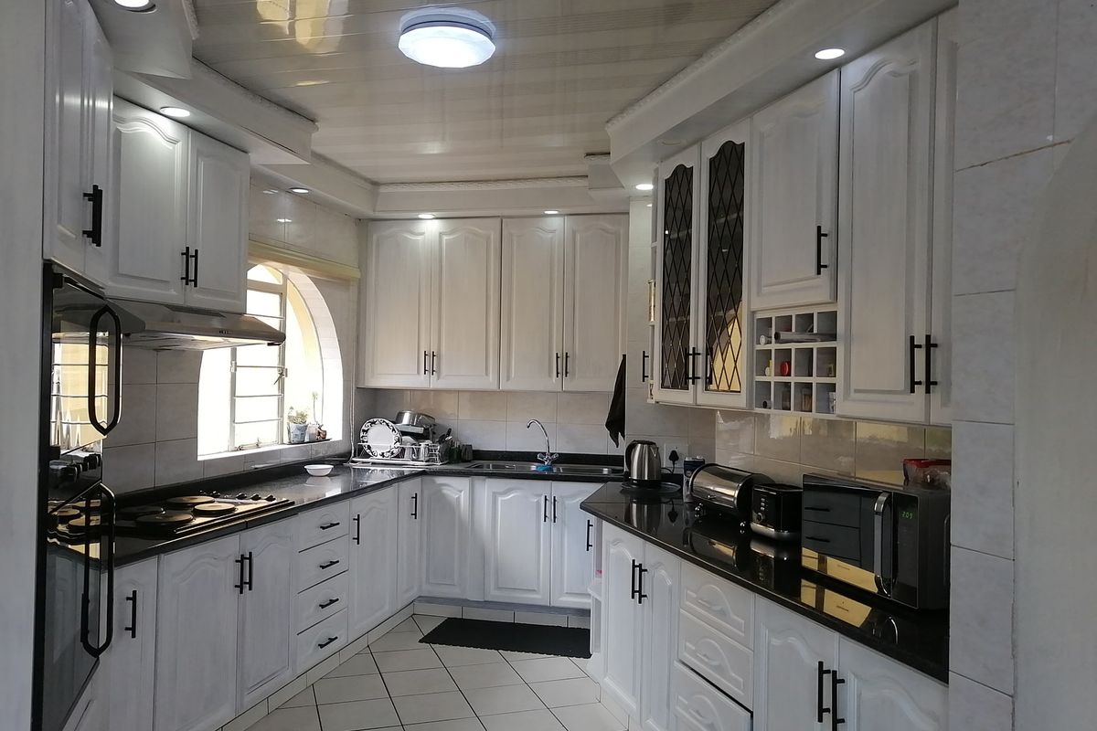 A well-maintained kitchen featuring white cabinetry, dark granite countertops, a built-in oven, hob, extractor fan, and tiled flooring.