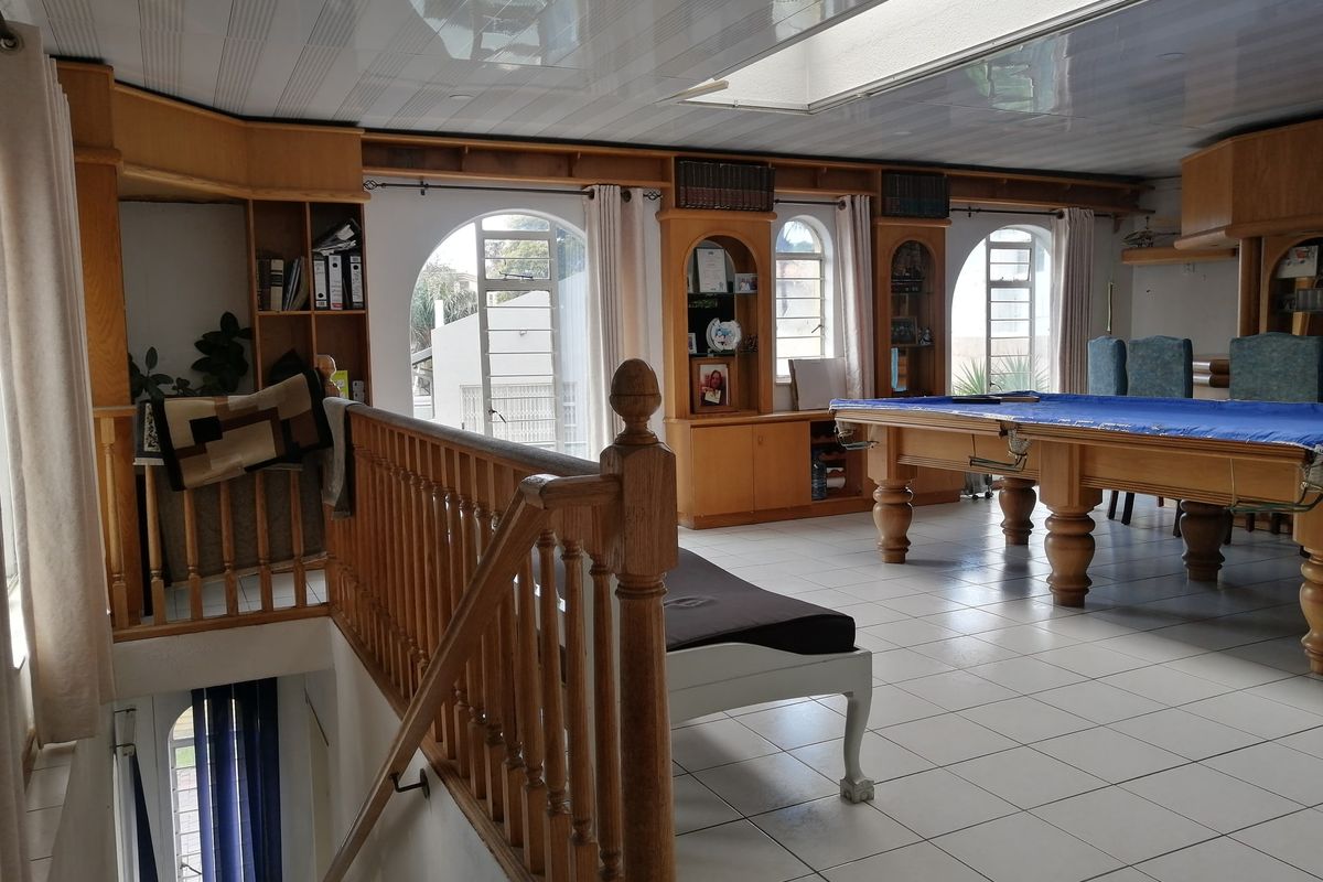 Spacious living area featuring built-in wooden cabinetry, arched windows, and a staircase with a wooden balustrade, offering a versatile layout for entertainment.