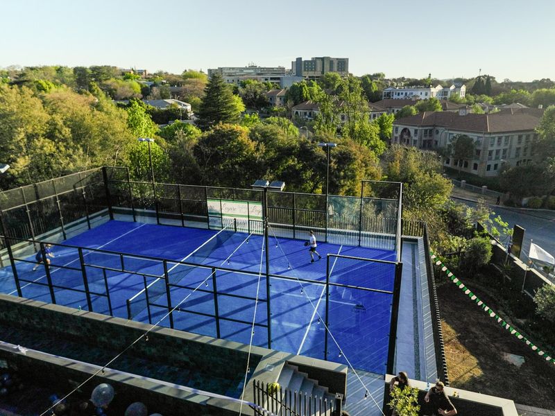 Aerial view of a modern, well-maintained padel court facility with integrated floodlighting, situated within a residential complex.