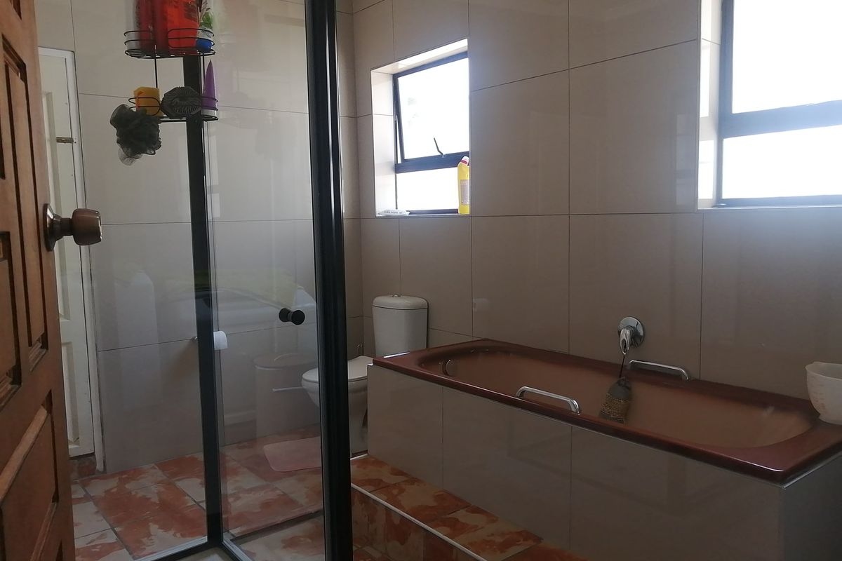 A functional bathroom featuring a built-in bathtub, a separate glass-enclosed shower, and a toilet with neutral wall tiling.