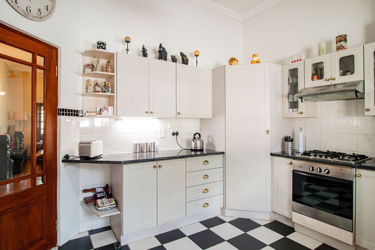 A well-maintained kitchen featuring classic white cabinetry, granite countertops, a gas hob, and distinctive black and white checkered floor tiles.