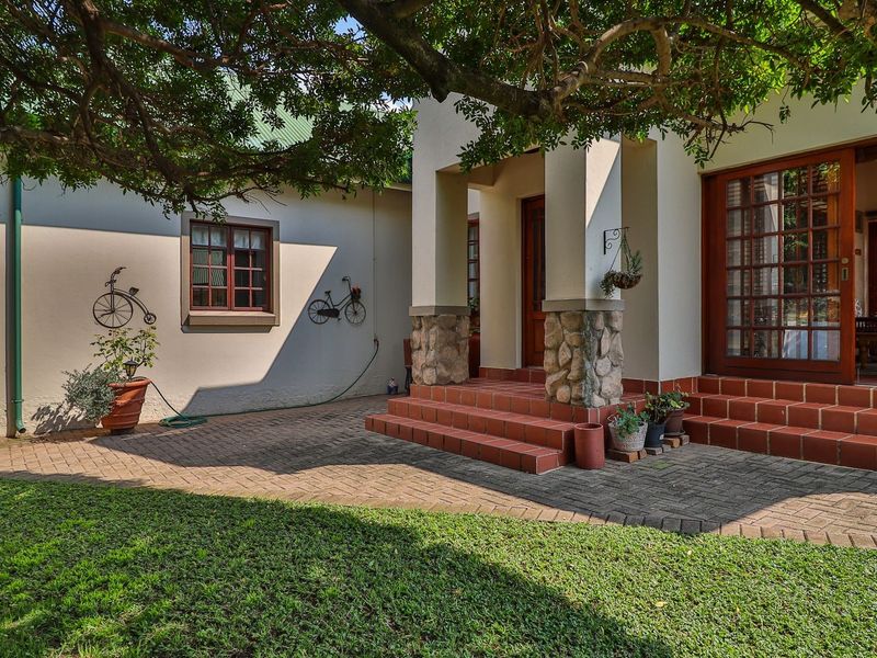 A well-maintained rear exterior featuring a paved patio, stone-clad pillars, terracotta tiled steps, and timber-framed glass doors leading into the home.