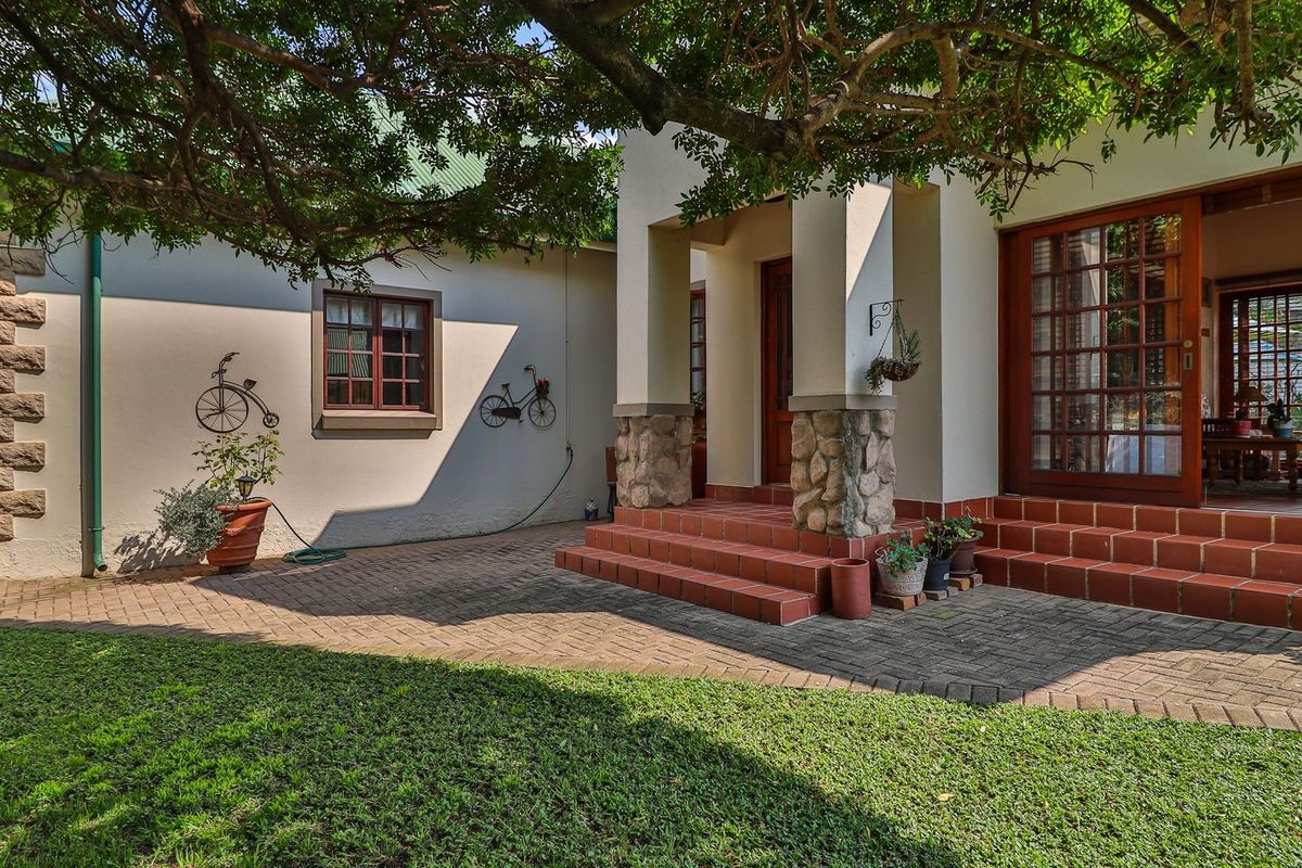 A well-maintained rear exterior featuring a paved patio, stone-clad pillars, terracotta tiled steps, and timber-framed glass doors leading into the home.