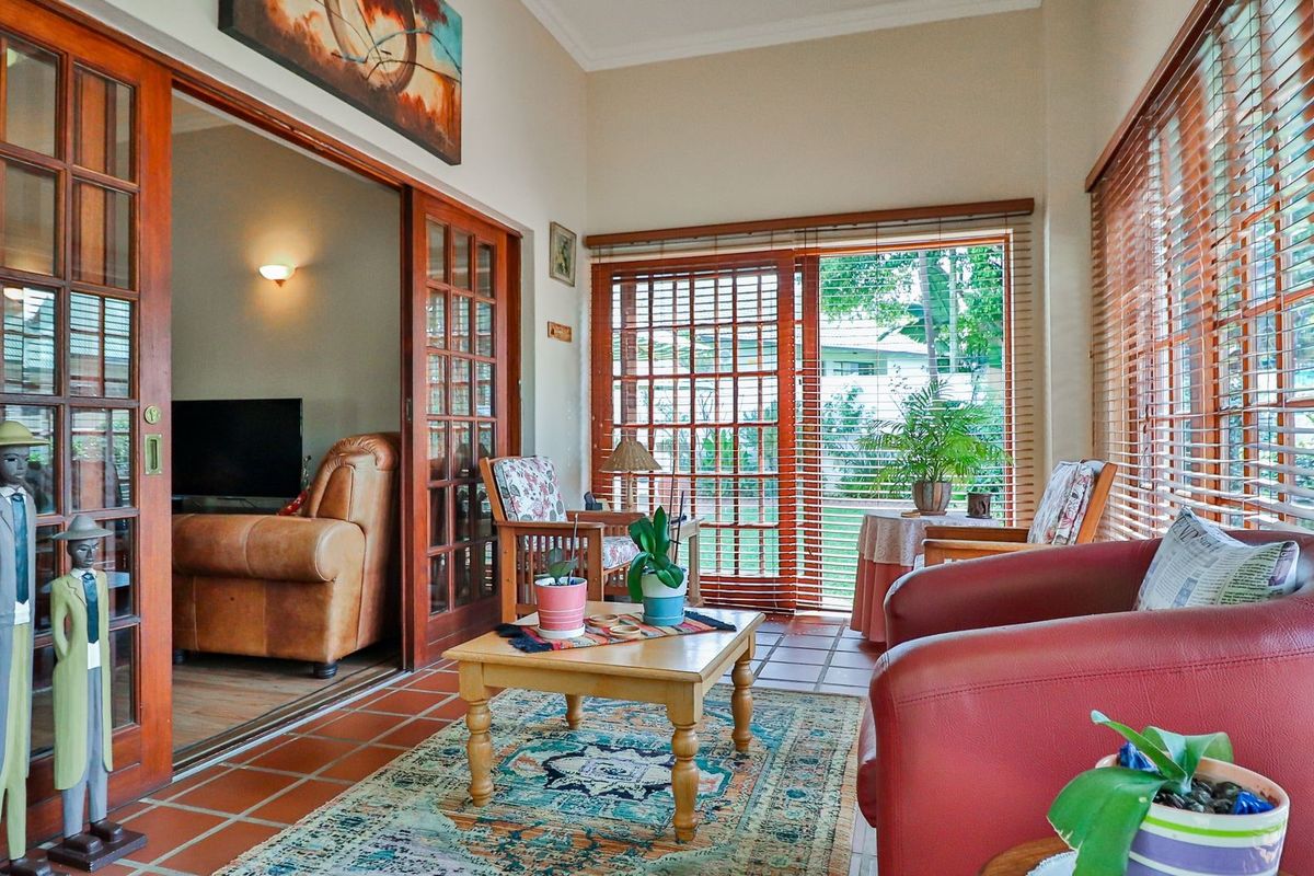 A sun-filled living area featuring terracotta floor tiles, extensive wooden sliding doors, and large windows with wooden blinds, offering a warm and inviting atmosphere.