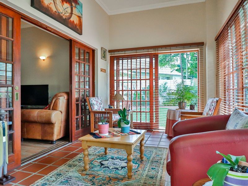 A sun-filled living area featuring terracotta floor tiles, extensive wooden sliding doors, and large windows with wooden blinds, offering a warm and inviting atmosphere.