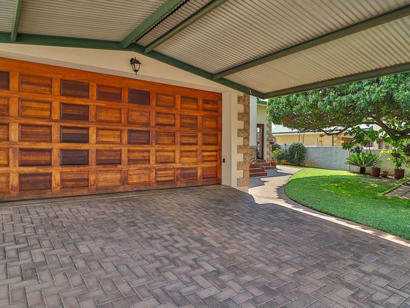 A well-maintained garage featuring a timber door, covered carport area, and paved driveway, set alongside a landscaped garden.