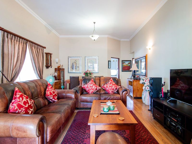 Spacious living room featuring warm hardwood flooring, elegant cove cornicing, and ambient wall sconce lighting, creating a comfortable and inviting atmosphere.