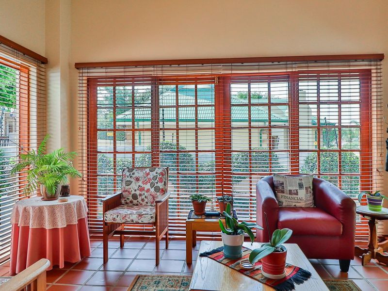 A bright living area featuring terracotta floor tiles and large wooden-framed glass sliding doors with venetian blinds, offering views of the garden.