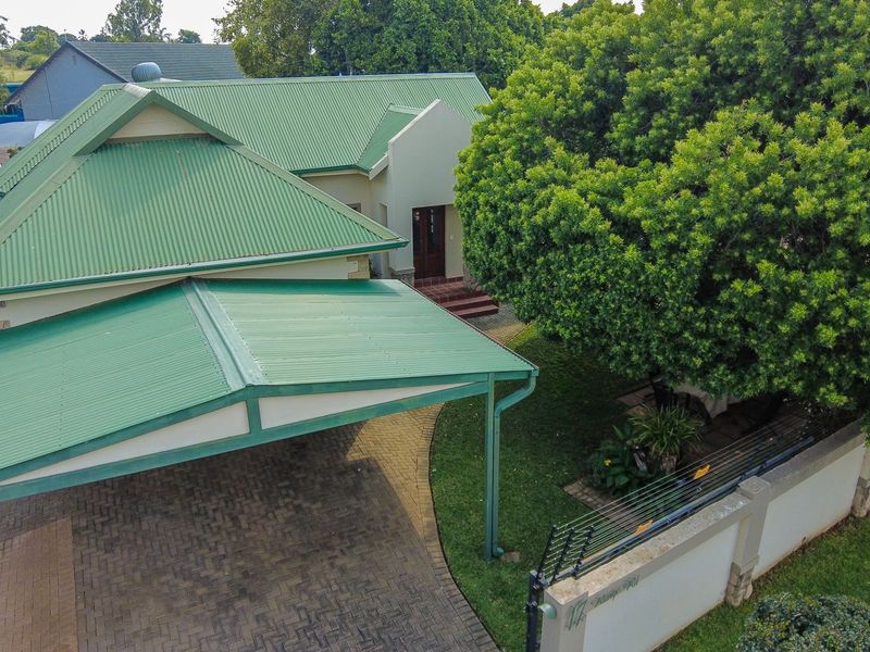 Aerial view of a residential property featuring a green corrugated metal roof, paved driveway, carport, and established garden with perimeter security fencing.