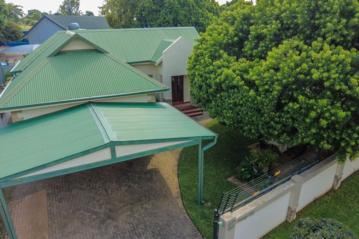 Aerial view of a residential property featuring a green corrugated metal roof, paved driveway, carport, and established garden with perimeter security fencing.