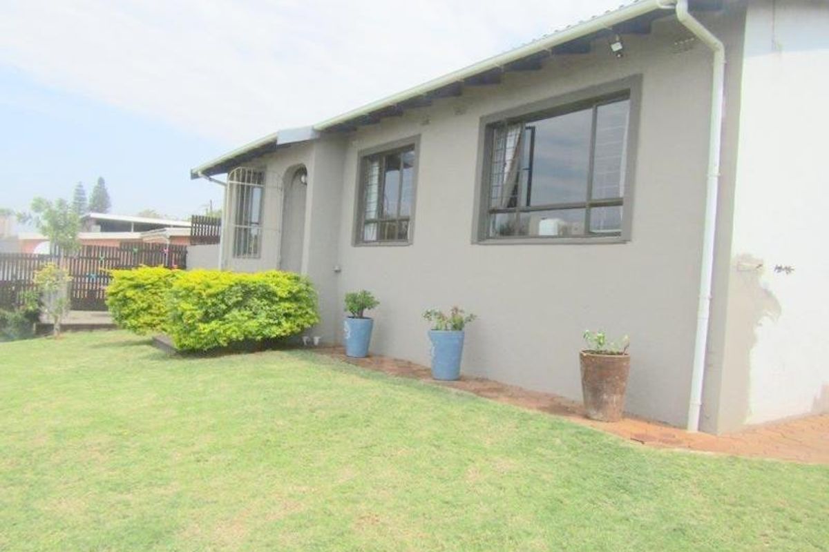 Rear exterior view of the house featuring plastered walls, aluminium window frames with security bars, and a well-maintained lawn area.