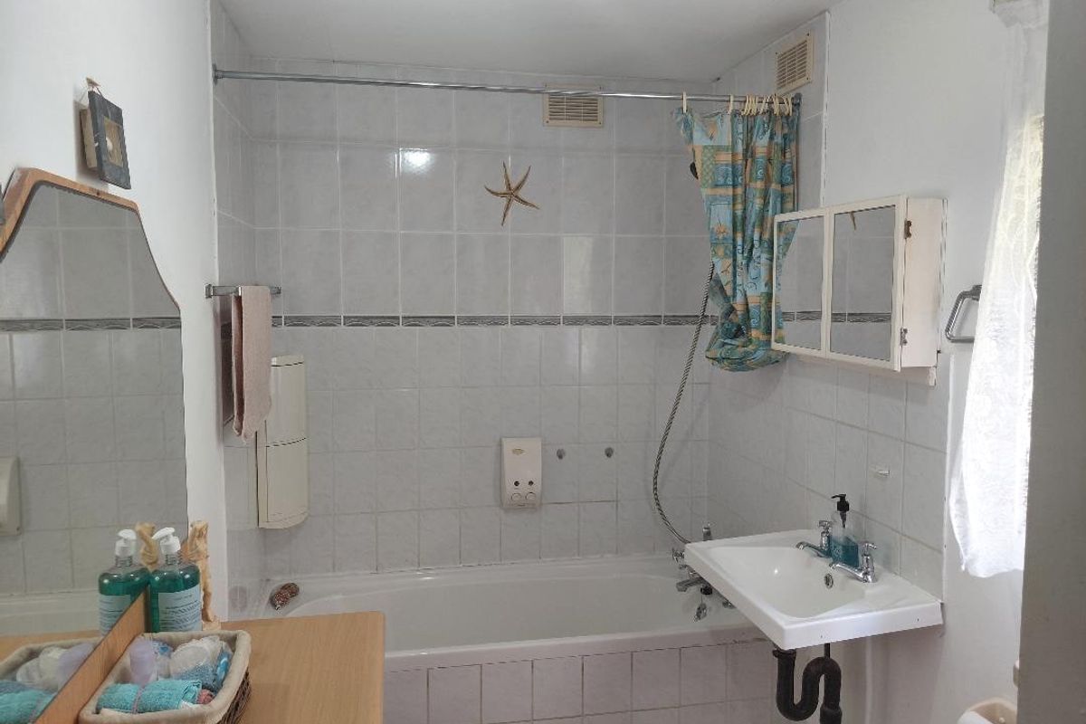 A functional bathroom featuring a bathtub with shower attachment, wall-mounted basin, and tiled wall finishes, offering potential for modernization.