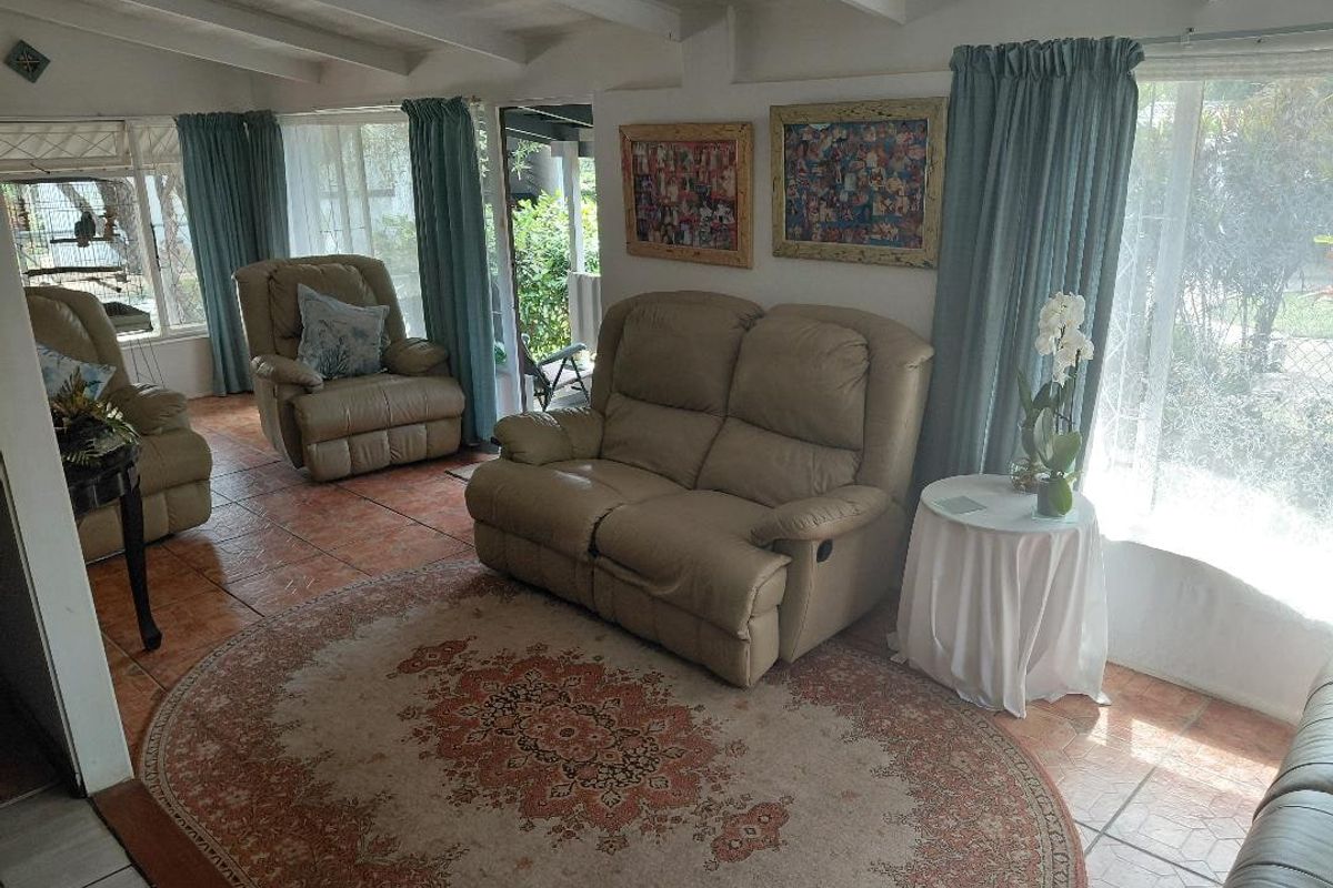 A sunlit living room featuring exposed beam ceilings and terracotta floor tiles, offering a bright and comfortable space with direct access to the garden.