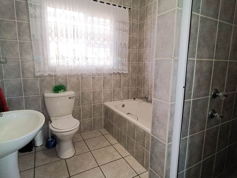 A functional bathroom featuring a pedestal basin, toilet, built-in bathtub, and a separate shower enclosure with neutral grey wall and floor tiling.