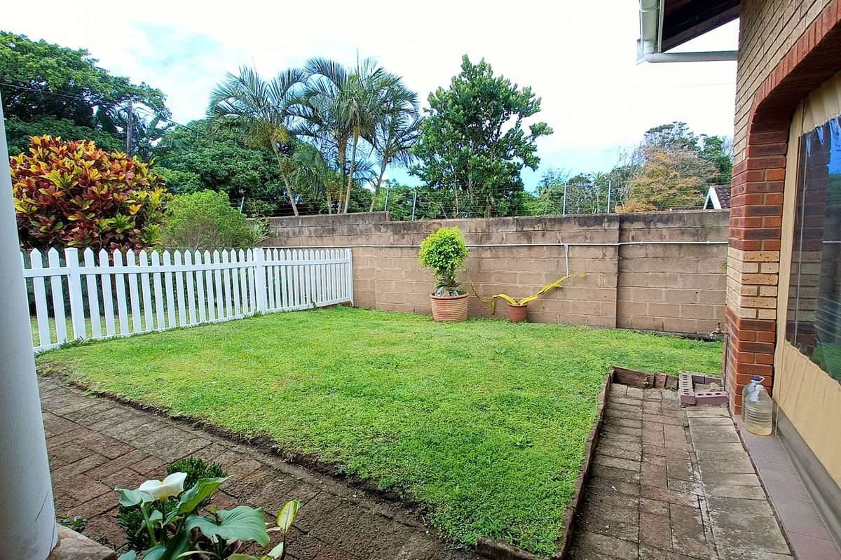 A private rear garden featuring a paved patio area, a well-maintained lawn, and a secure brick boundary wall.