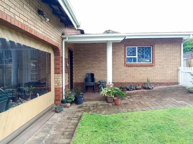 A covered brick patio area featuring paved flooring and a white picket fence, providing a functional outdoor space for relaxation.