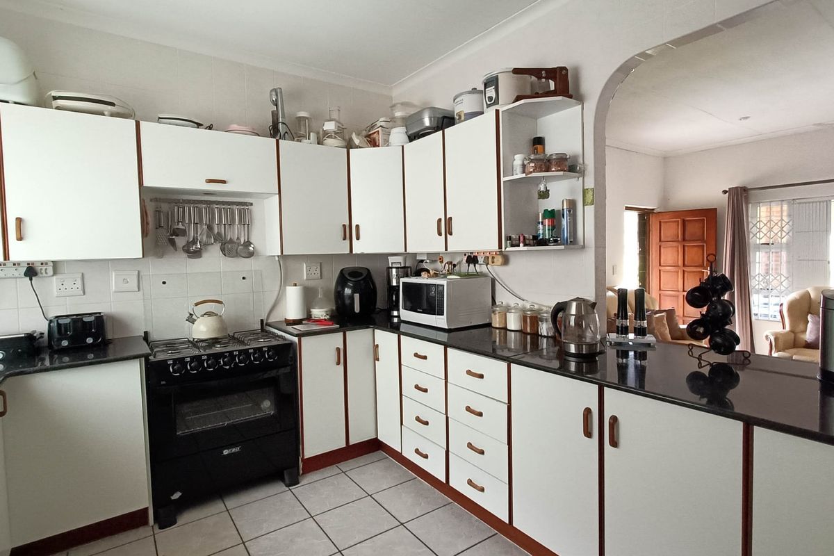 A functional kitchen featuring white cabinetry, dark granite countertops, a gas stove, and tiled flooring, with an open-plan layout leading to the living area.