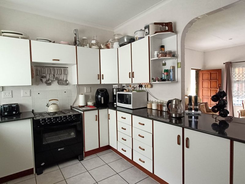 A functional kitchen featuring white cabinetry, dark granite countertops, a gas stove, and tiled flooring, with an open-plan layout leading to the living area.