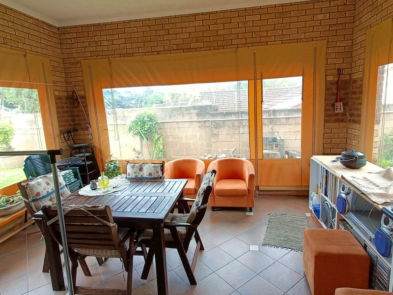 Enclosed patio area featuring exposed brick walls, tiled flooring, and roll-down outdoor blinds, providing a versatile space for outdoor living and dining.
