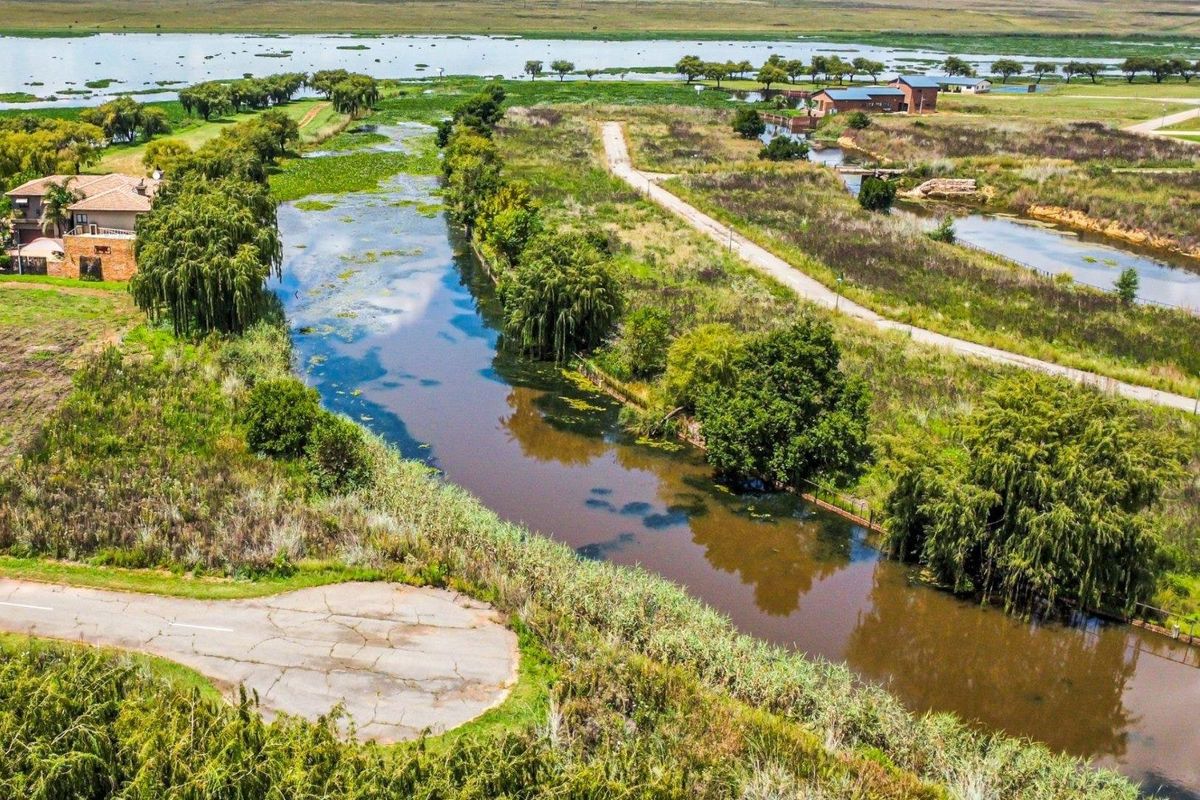 Aerial view of a residential land plot featuring a natural waterway, surrounding greenery, and access to a paved road.