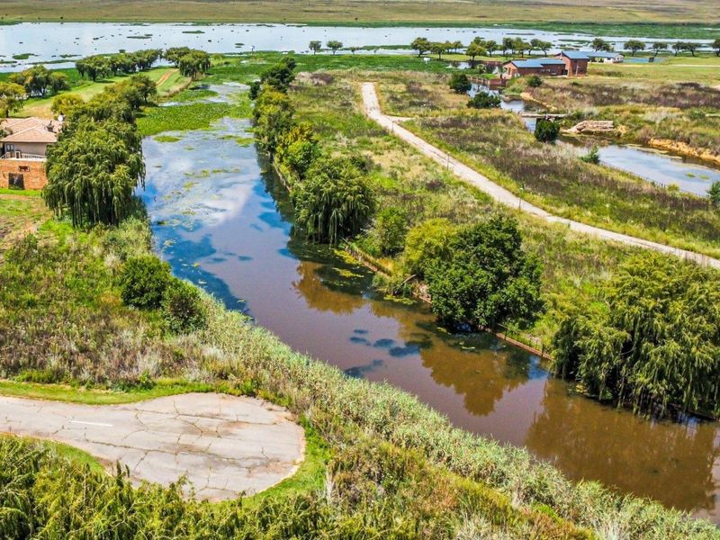 Aerial view of a residential land plot featuring a natural waterway, surrounding greenery, and access to a paved road.