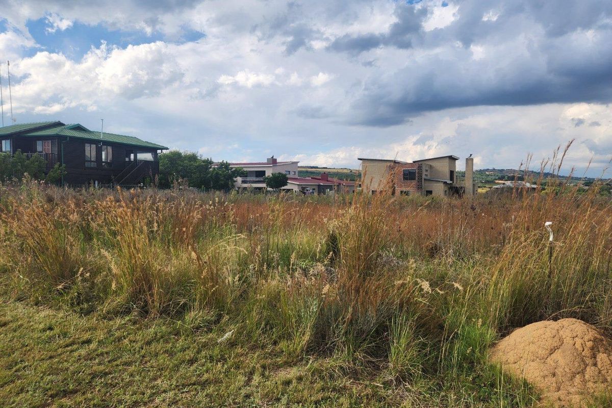 A view of a vacant residential plot featuring natural grass and vegetation, with neighboring houses visible in the background.