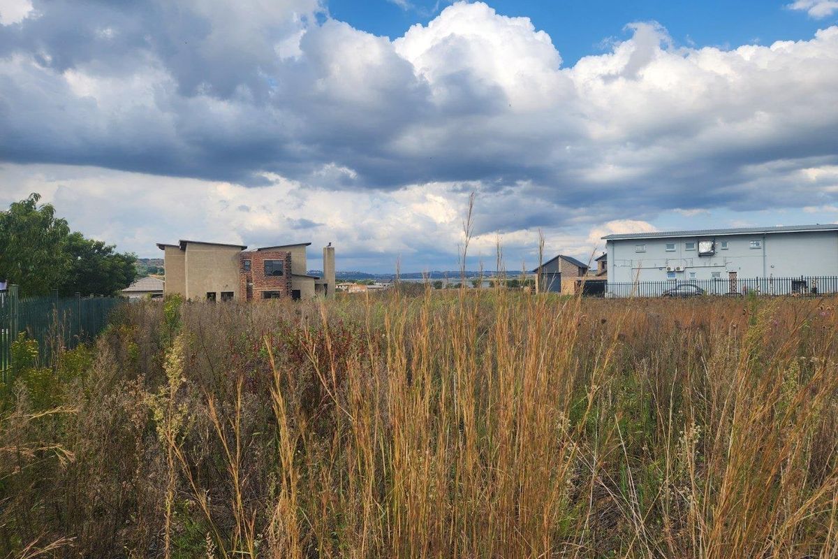 A view of a vacant residential plot featuring overgrown grass with neighboring properties visible in the background.